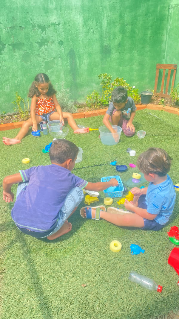 Crianças brincando com água e baldinhos na grama do quintal